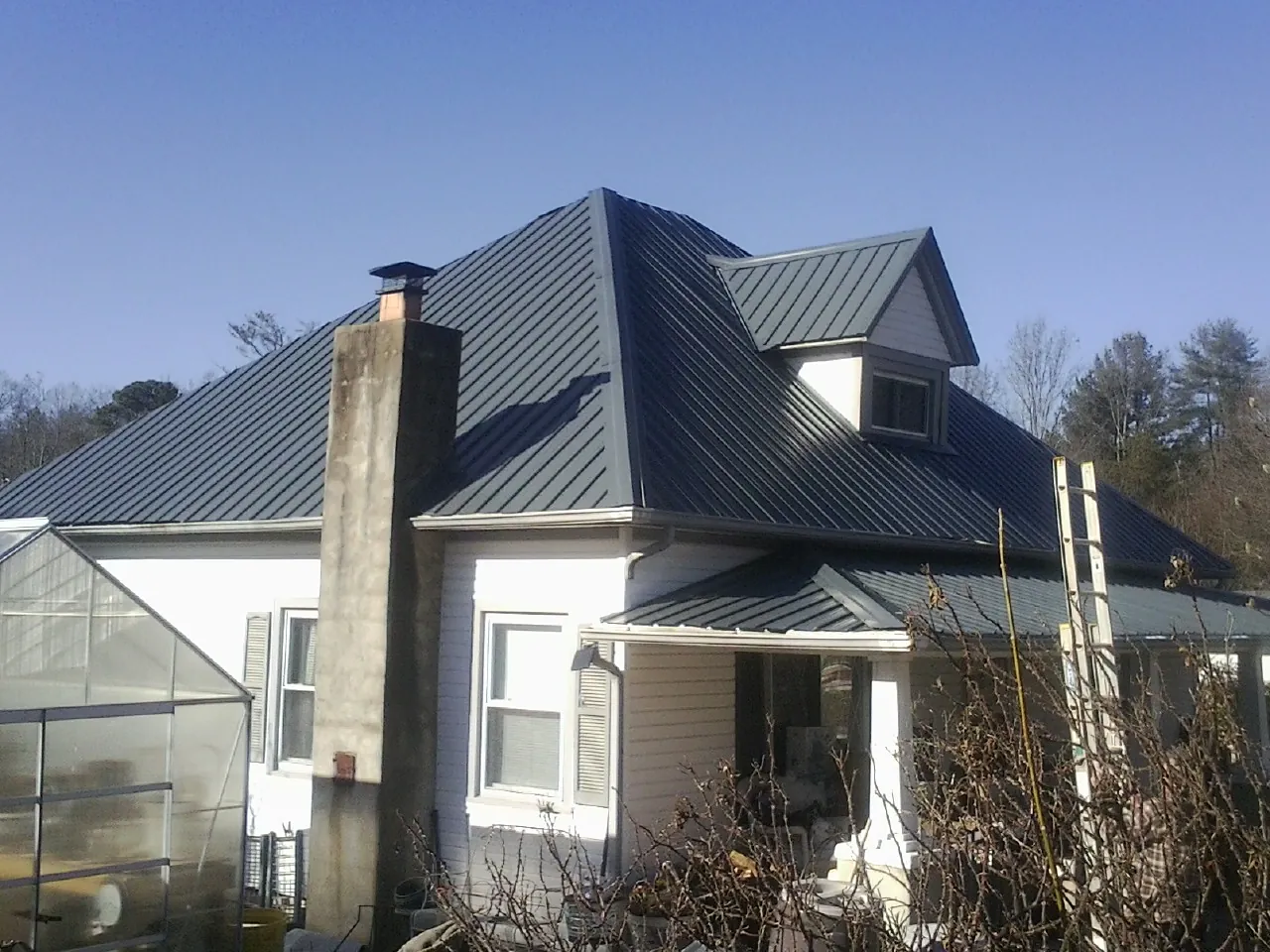 Dark blue standing seam metal roof on a white farmhouse with dormer — Slate & Tile Roof Repair by Roofing Brothers in Seven Mile
