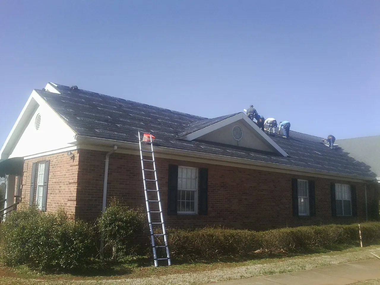 Crew tearing shingles off a brick ranch roof with a ladder set — Emergency Roof Repair work by our crew in Seven Mile
