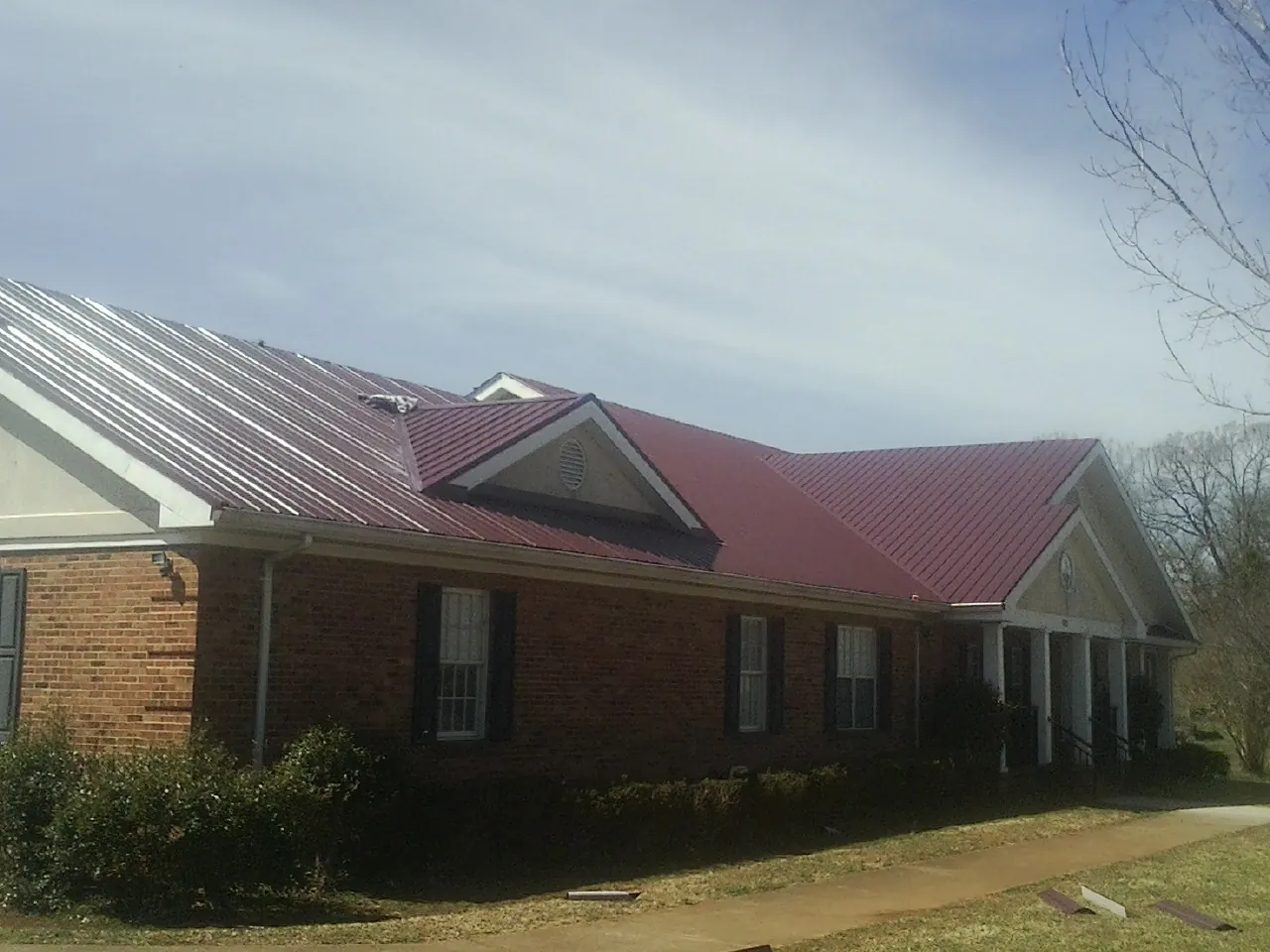 Red metal roof with gabled entries on a long brick building, from a Hail Damage Roof Repair job in Seven Mile