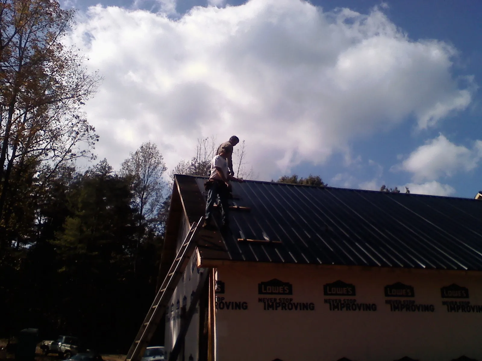 Roofer fastening dark metal panels high against a cloudy sky, from a Roof Inspection job in Seven Mile