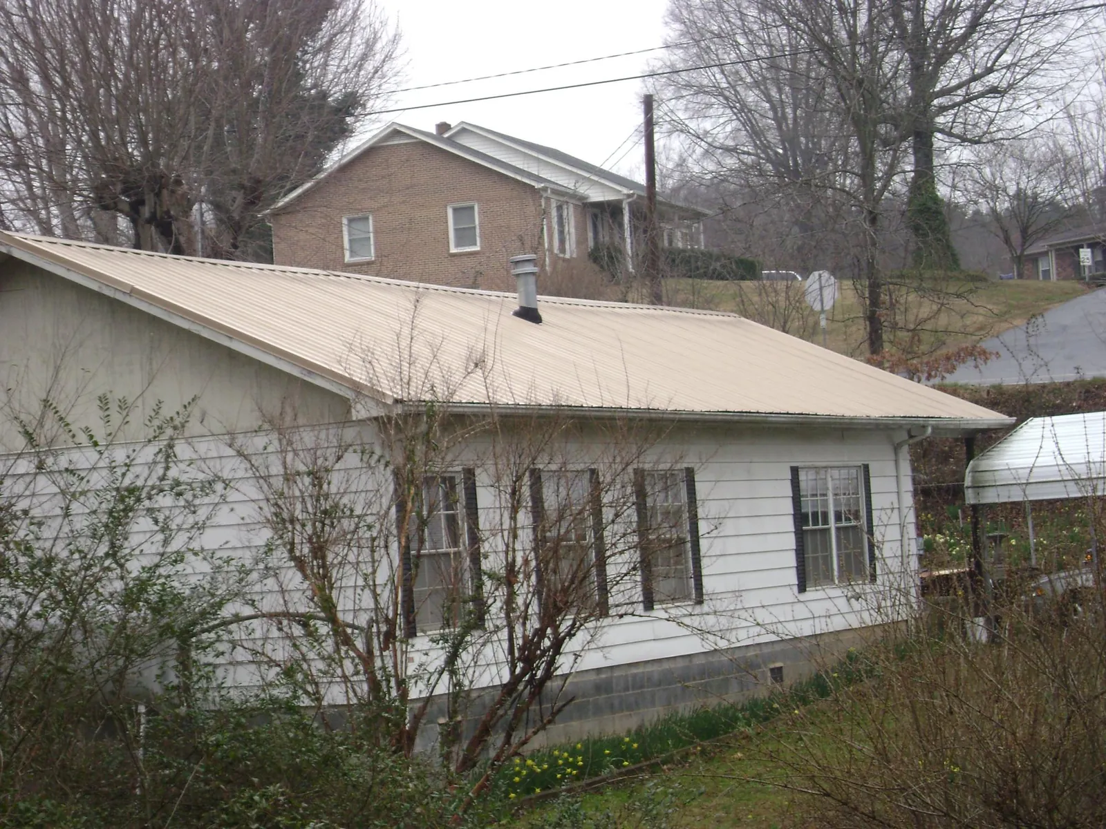 Tan metal roof on a white sided house set into a hillside — Commercial Roofing by Roofing Brothers in Seven Mile
