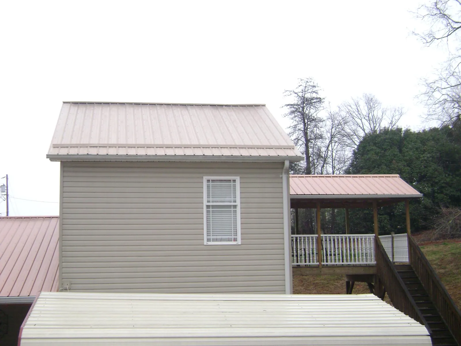 Tan metal roofs on a two story addition and attached porch, from a Roof Replacement job in Seven Mile